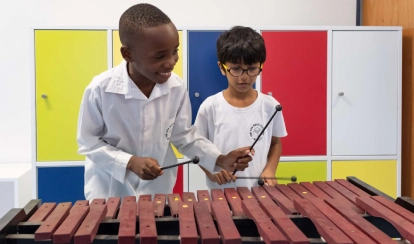 A group of students at AKA Dhaka sit around a table in the art studio, painting vibrant artworks on canvas with brushes and pastels.